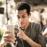 Young man wearing headphones, engaging in a video call outdoors on a sunny day.