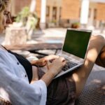 Relaxing professional woman working on a laptop outdoors by the poolside.