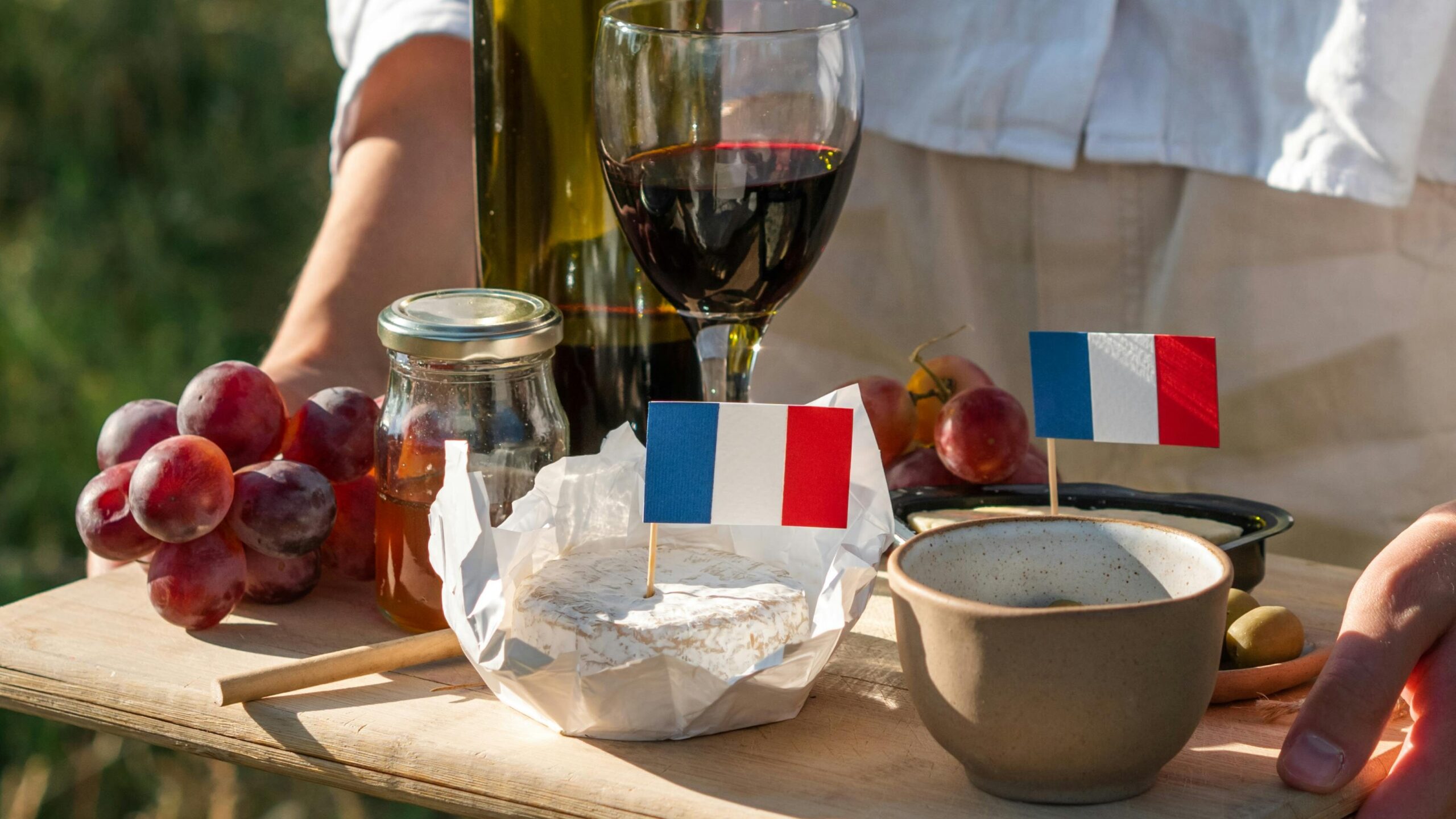 A beautiful outdoor French picnic setup featuring wine, cheese, and grapes with French flags.